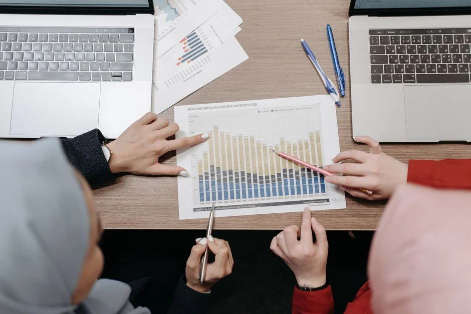 A modern workspace showing hands analyzing marketing data on a laptop and paper documents.